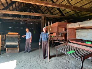 Miniatura zdjęcia: dwóch panów w stodole ogląda stare maszyny